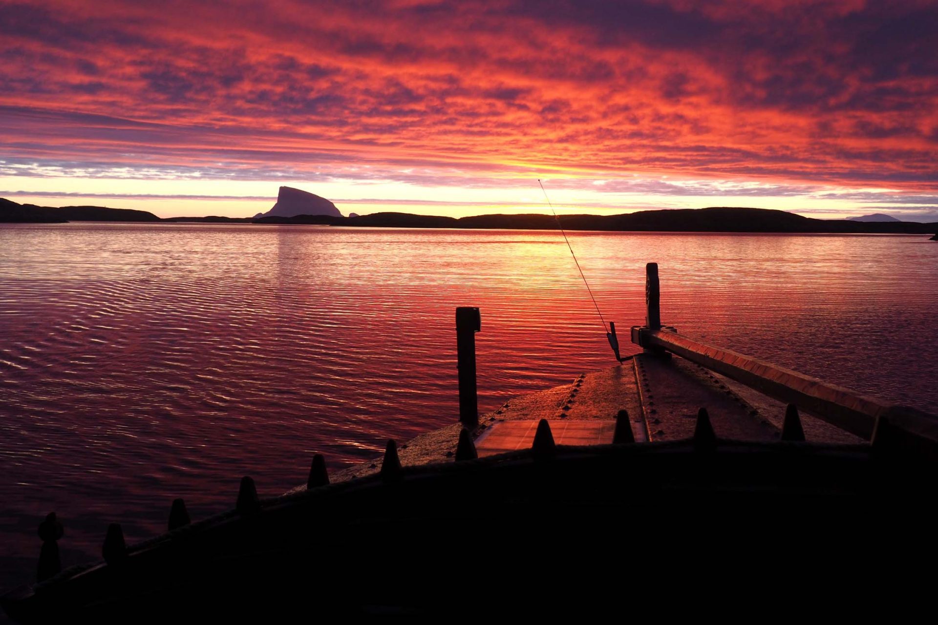 Seiltur-Helgeland-Lovund-trebat Seiling i solnedgang pa helgelandskysten. Trebat med rorgrind i forgrunnen, Lovund i bakgrunnen.