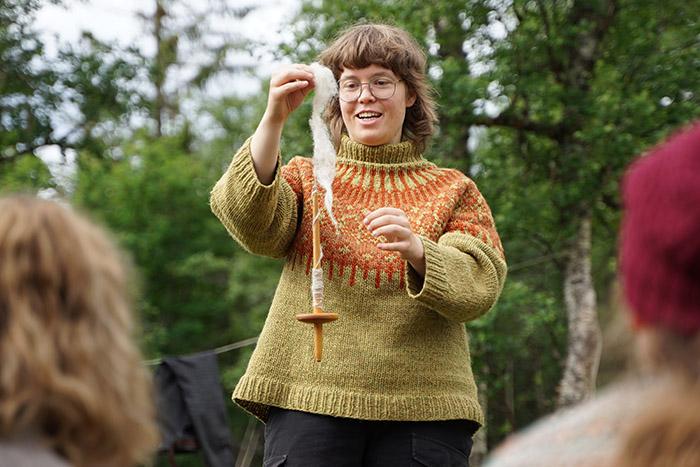 A woman spinning on a drop spindle outdoors