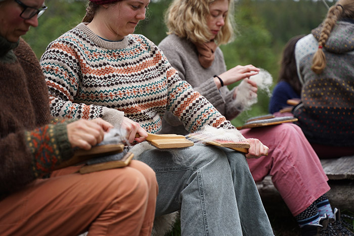 A group of people sitting outside carding wool
